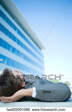 Businessman lying on ground outdoors, hands behind head, cropped view View Large Photo Image Stock Photo - Businessman lying on ground outdoors, hands behind head, cropped view. Fotosearch
