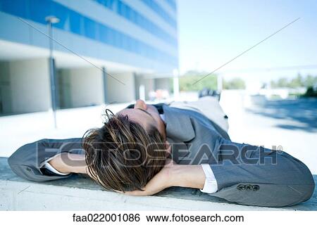 Businessman lying on ground outdoors, hands behind head, full length View Large Photo Image Stock Photograph - Businessman lying on ground outdoors, hands behind head, full length. Fotosearch