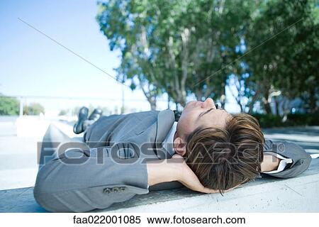 Stock Photography - Businessman lying on ground outdoors, hands behind head, full length. Fotosearch