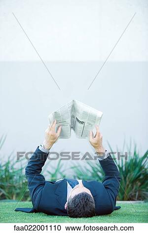 Businessman lying on the ground outdoors, reading newspaper View Large Photo Image Stock Image - Businessman lying on the ground outdoors, reading newspaper. Fotosearch