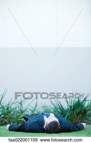Businessman lying on the ground outdoors, wearing full suit View Large Photo Image Stock Photo - Businessman lying on the ground outdoors, wearing full suit. Fotosearch