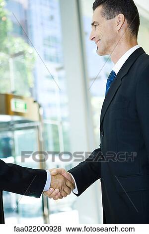 Stock Photo - Businessman shaking associate's hand, smiling, cropped view. Fotosearch