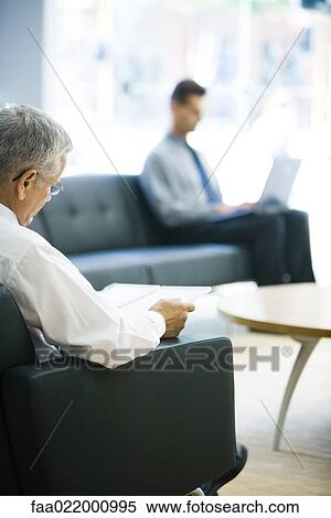 Businessman sitting in waiting room, reading file, man using laptop in background View Large Photo Image Stock Photography - Businessman sitting in waiting room, reading file, man using laptop in background. Fotosearch