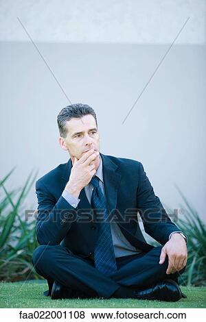 Businessman sitting on the ground outdoors, looking away, finger on lips View Large Photo Image Stock Photo - Businessman sitting on the ground outdoors, looking away, finger on lips. Fotosearch