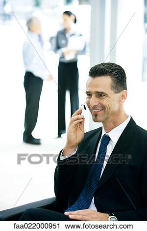 Businessman sitting, using cell phone, smiling View Large Photo Image Stock Image - Businessman sitting, using cell phone, smiling. Fotosearch
