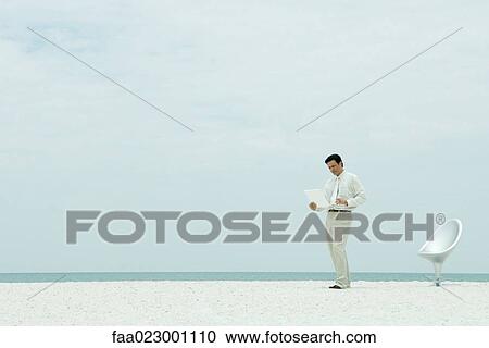 Businessman standing on beach, looking at laptop computer, full length View Large Photo Image Stock Image - Businessman standing on beach, looking at laptop computer, full length. Fotosearch