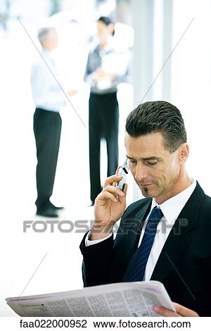 Businessman using cell phone, looking at newspaper View Large Photo Image Stock Image - Businessman using cell phone, looking at newspaper. Fotosearch