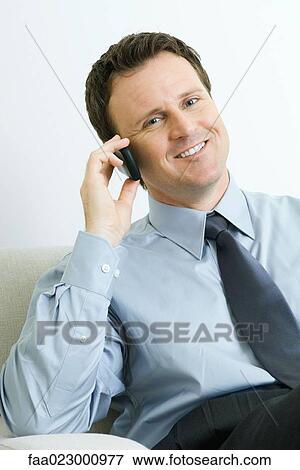 Stock Photo - Businessman using cell phone, smiling at camera, portrait. Fotosearch