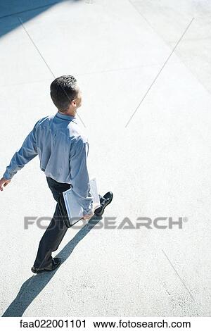 Stock Image - Businessman walking outdoors, full length, high angle view. Fotosearch