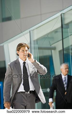Businessman walking, using cell phone, looking away, building in background View Large Photo Image Stock Photo - Businessman walking, using cell phone, looking away, building in background. Fotosearch