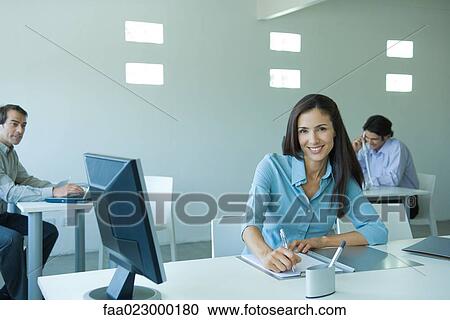 Businesswoman sitting at desk, smiling at camera View Large Photo Image Stock Image - Businesswoman sitting at desk, smiling at camera. Fotosearch