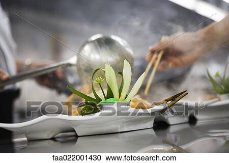 Stock Image - Chefs dressing plates in commercial kitchen. Fotosearch