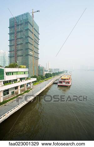 China, Guangdong Province, barge parked along quay near high rise under construction View Large Photo Image Stock Photo - China, Guangdong Province, barge parked along quay near high rise under construction. Fotosearch