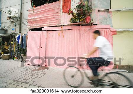 Picture - China, Guangdong Province, Guangzhou, man riding bicycle through street. Fotosearch