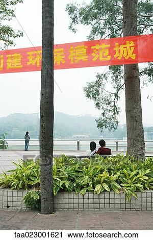 China, Guangdong Province, Guangzhou, couple sitting on bench near water, looking at view, rear view View Large Photo Image Stock Image - China, Guangdong Province, Guangzhou, couple sitting on bench near water, looking at view, rear view. Fotosearch