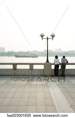 Stock Image - China, Guangdong Province, Guangzhou, couple looking at view over river, rear view. Fotosearch