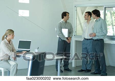 Colleagues working in office, three men standing by window while woman sits at desk, pointing to document View Large Photo Image Stock Image - Colleagues working in office, three men standing by window while woman sits at desk, pointing to document. Fotosearch