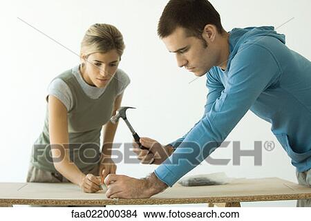 Couple hammering nail into fiberboard panel View Large Photo Image Picture - Couple hammering nail into fiberboard panel. Fotosearch