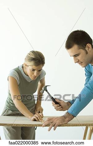 Stock Photography - Couple hammering nail into fiberboard panel. Fotosearch
