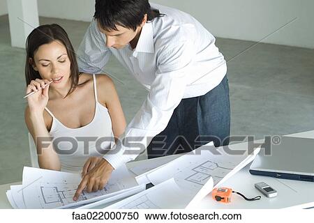 Couple looking at blueprints together, man looking over woman's shoulder, pointing to blueprint View Large Photo Image Stock Image - Couple looking at blueprints together, man looking over woman's shoulder, pointing to blueprint. Fotosearch