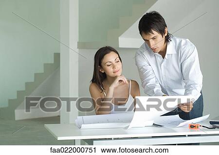 Couple looking at blueprints together, man leaning over table, holding up blueprint View Large Photo Image Stock Image - Couple looking at blueprints together, man leaning over table, holding up blueprint. Fotosearch