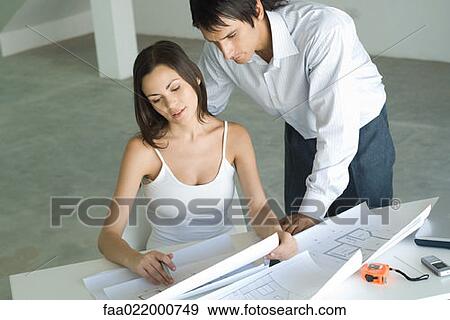 Couple looking at blueprints together, man looking over woman's shoulder View Large Photo Image Stock Photo - Couple looking at blueprints together, man looking over woman's shoulder. Fotosearch