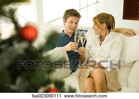 Couple making a toast with champagne, smiling at each other, Christmas tree in foreground View Large Photo Image Stock Image - Couple making a toast with champagne, smiling at each other, Christmas tree in foreground. Fotosearch
