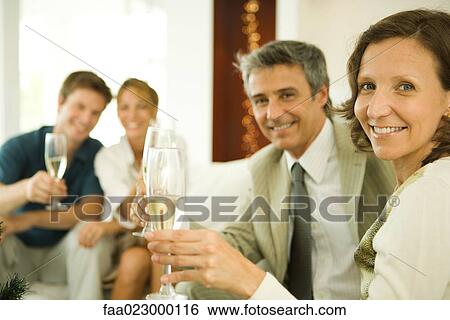 Couple making a toast with champagne, smiling at camera, friends in background View Large Photo Image Stock Photograph - Couple making a toast with champagne, smiling at camera, friends in background. Fotosearch