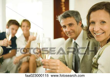 Couple making a toast with champagne, smiling at camera, friends in background View Large Photo Image Stock Photography - Couple making a toast with champagne, smiling at camera, friends in background. Fotosearch