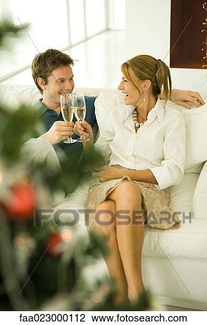 Couple making toast with champagne, smiling at each other, Christmas tree in foreground View Large Photo Image Stock Image - Couple making toast with champagne, smiling at each other, Christmas tree in foreground. Fotosearch