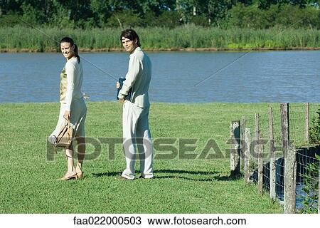 Couple outdoors, woman holding purse and man holding laptop, both looking over shoulders, smiling at camera View Large Photo Image Stock Image - Couple outdoors, woman holding purse and man holding laptop, both looking over shoulders, smiling at camera. Fotosearch