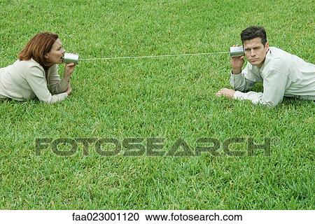 Couple reclining on the ground, talking to each other through tin can phone View Large Photo Image Stock Image - Couple reclining on the ground, talking to each other through tin can phone. Fotosearch