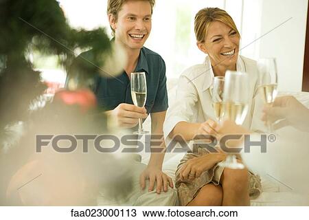 Couple sitting on couch, making a toast with champagne, smiling at friends View Large Photo Image Stock Image - Couple sitting on couch, making a toast with champagne, smiling at friends. Fotosearch