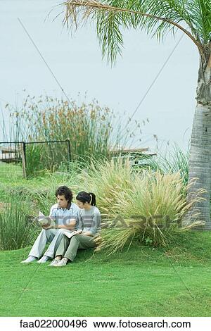 Couple sitting on grass, reading books View Large Photo Image Stock Photograph - Couple sitting on grass, reading books. Fotosearch