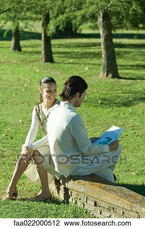 Couple sitting outdoors on low wall, man reading newspaper View Large Photo Image Stock Image - Couple sitting outdoors on low wall, man reading newspaper. Fotosearch