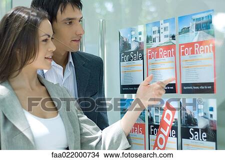 Picture - Couple standing next to window of real estate agency, looking at for rent sign. Fotosearch