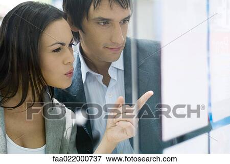 Stock Photo - Couple standing next to window of real estate agency, looking at for rent and for sale signs. Fotosearch
