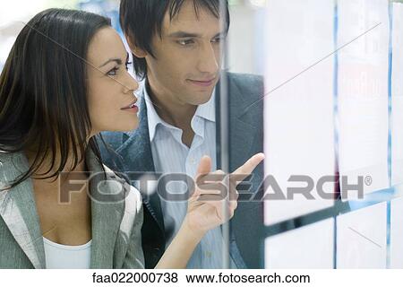 Stock Photo - Couple standing next to window of real estate agency, looking at for rent and for sale signs. Fotosearch
