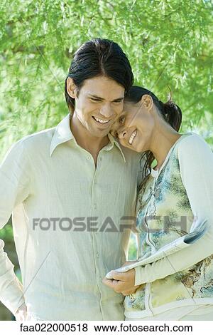 Stock Photo - Couple standing outdoors holding newspaper, woman resting head on man's shoulder. Fotosearch