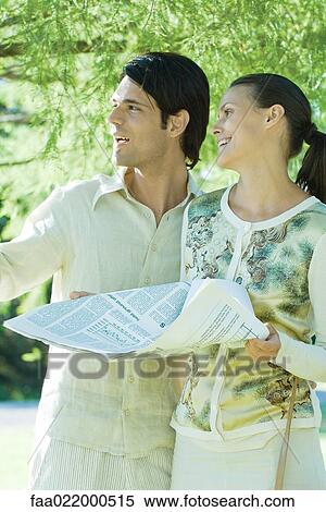 Couple standing outdoors holding newspaper, looking out of frame View Large Photo Image Stock Photography - Couple standing outdoors holding newspaper, looking out of frame. Fotosearch