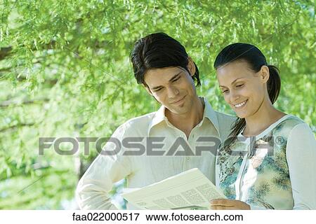 Couple standing outdoors reading newspaper View Large Photo Image Stock Photo - Couple standing outdoors reading newspaper. Fotosearch