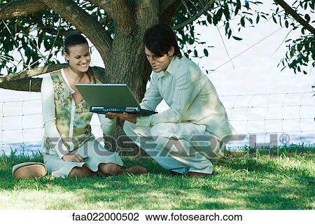 Couple under tree, man holding open laptop View Large Photo Image Stock Image - Couple under tree, man holding open laptop. Fotosearch
