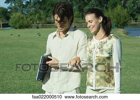 Stock Image - Couple walking arm in arm, man carrying laptop. Fotosearch