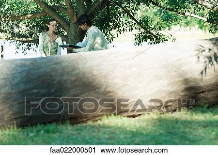 Couple with laptop, tree trunk in foreground View Large Photo Image Stock Image - Couple with laptop, tree trunk in foreground. Fotosearch