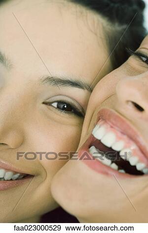 Cropped view of two young friends smiling at camera, cheek to cheek, extreme close-up View Large Photo Image Stock Photo - Cropped view of two young friends smiling at camera, cheek to cheek, extreme close-up. Fotosearch