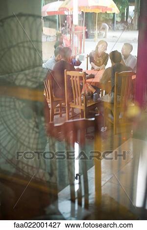 Stock Photo - Diners sitting at table outdoors, seen through window. Fotosearch