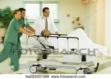 Stock Photo - Emergency room staff pushing man on stretcher, blurred motion. Fotosearch
