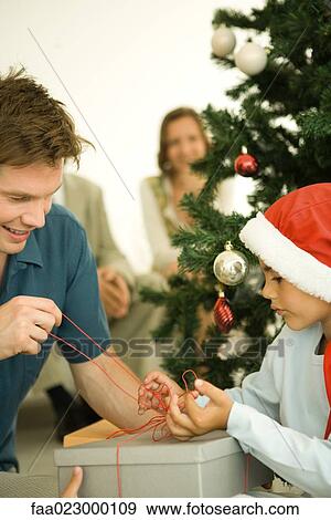 Stock Photo - Father and son opening present together by Christmas tree. Fotosearch