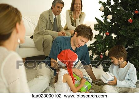Father and two children sitting by Christmas tree, opening presents together, family watching View Large Photo Image Stock Image - Father and two children sitting by Christmas tree, opening presents together, family watching. Fotosearch