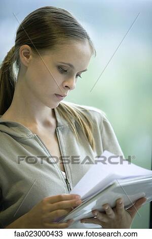 Stock Image - Female college student reading paper in binder, head and shoulders, portrait. Fotosearch